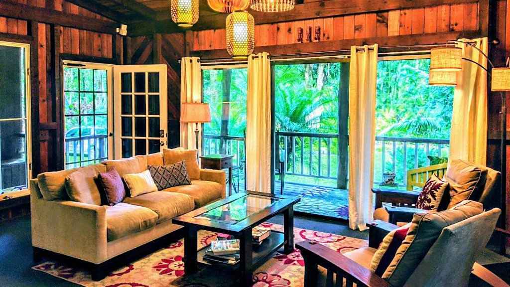 The cosy living room looking out over greenery at Kehena Mauka Nui Club, a clothing-option LGBTQIA+ resort in Hawaii!