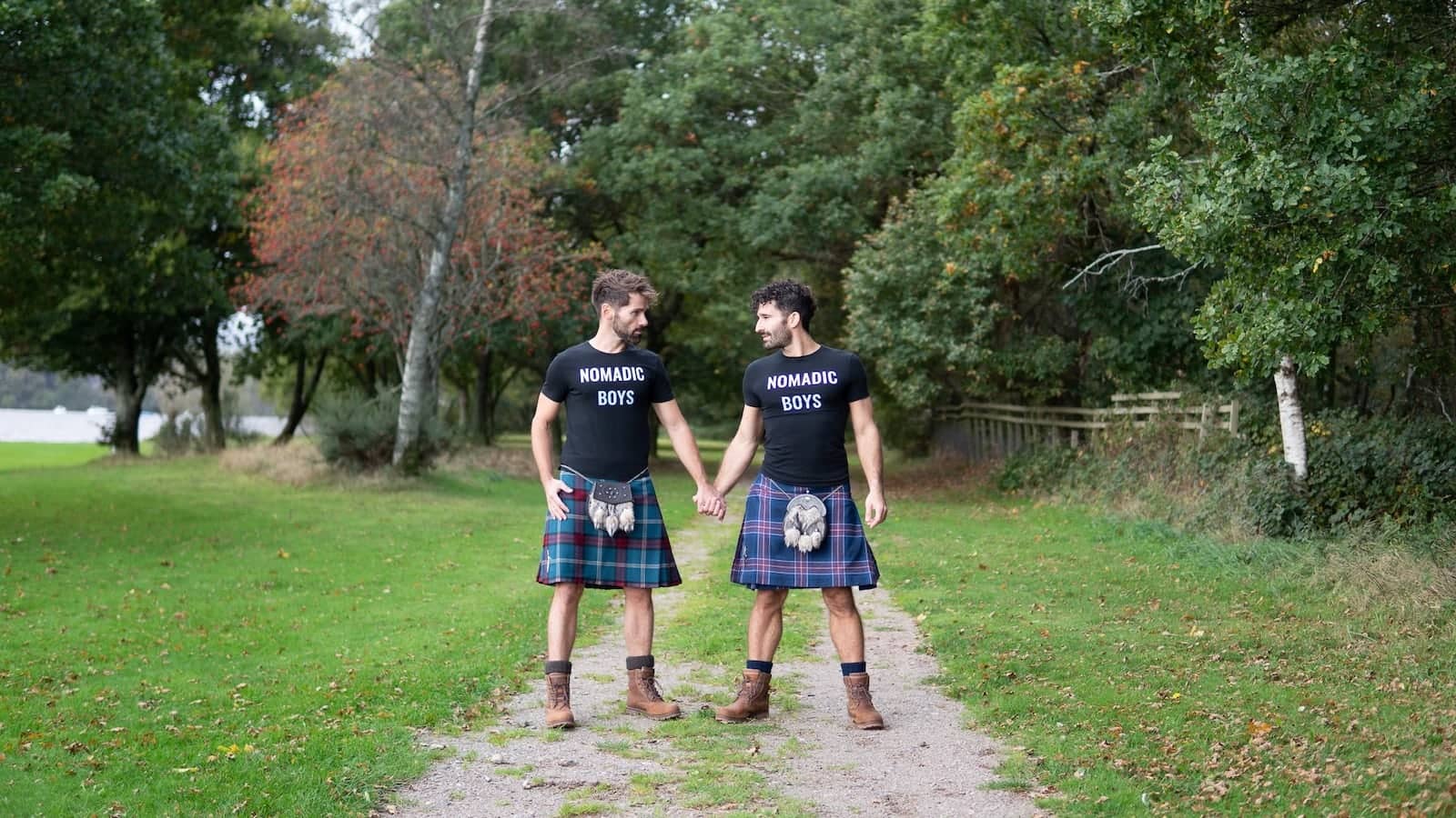 Nomadic Boys gay couple wearing branded t shirts with their kilt in Loch Lomond, Scotland.