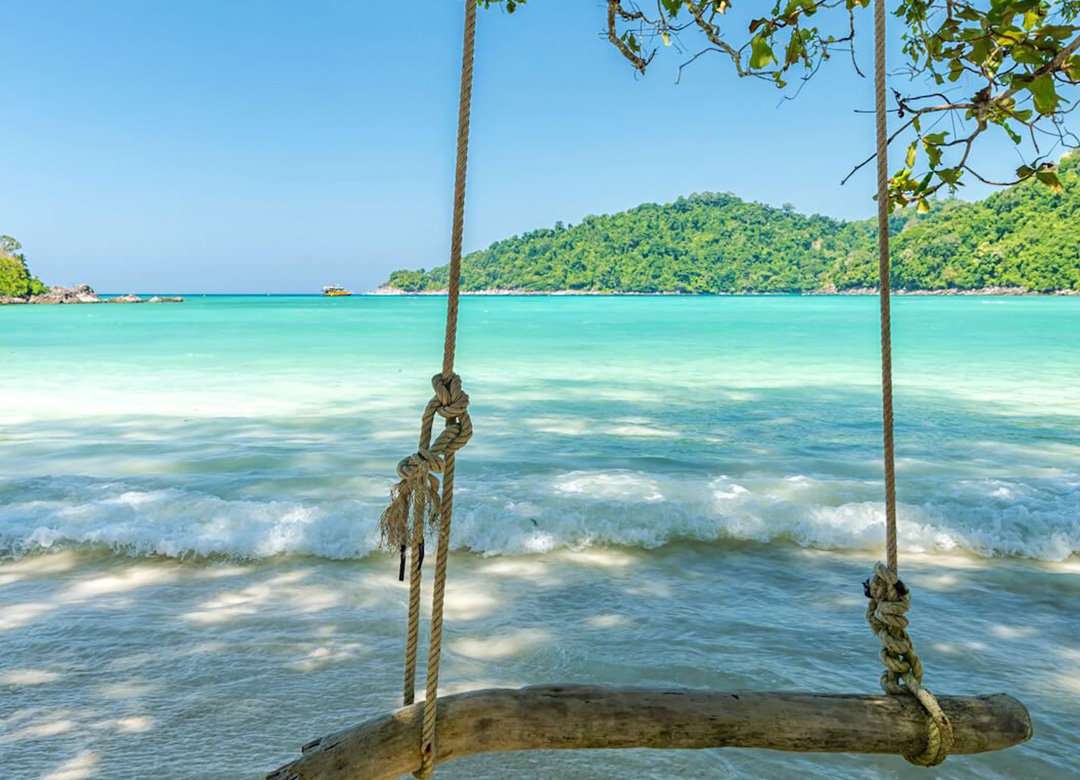 A view of Surin Beach in Phuket as seen from behind a rope and stick swing.