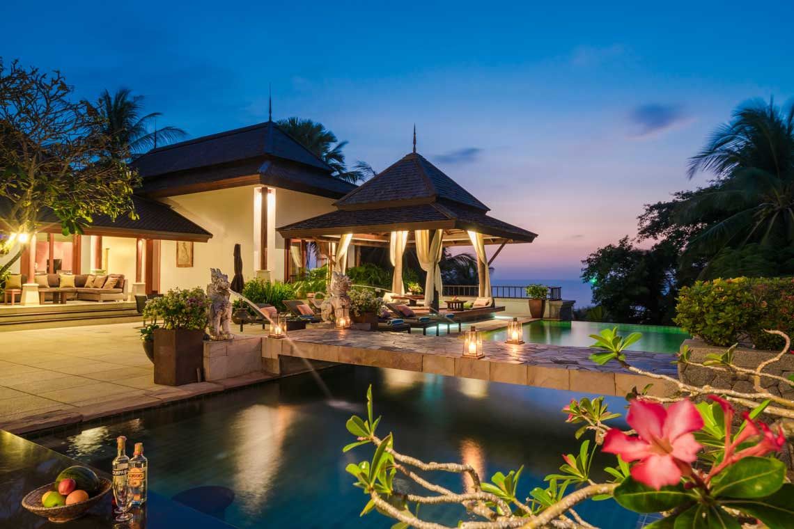 The beautiful Naked Thai Villa at dusk with a view of the pool and flowers in the foreground.