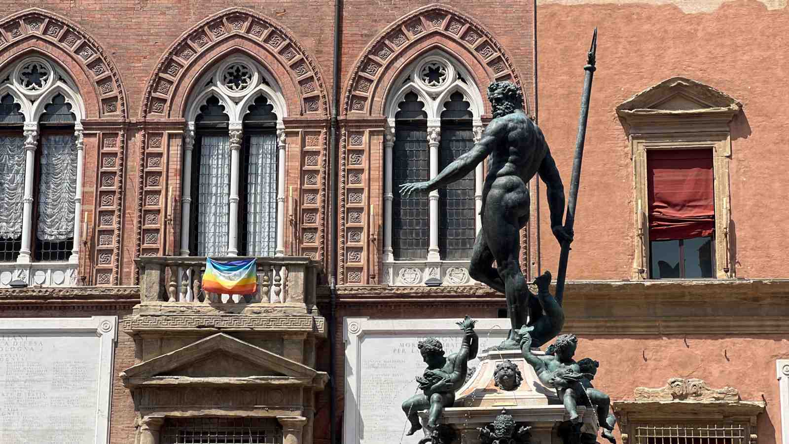 Neptuno statue in gay Bologna with rainbow flag behind it.