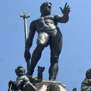 A low angle shot of a statue of Poseidon with blue sky behind.