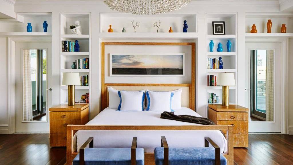 A hotel bedroom with a bed set into a wall framed by built-in shelving housing sculptures and books making it look very homey.
