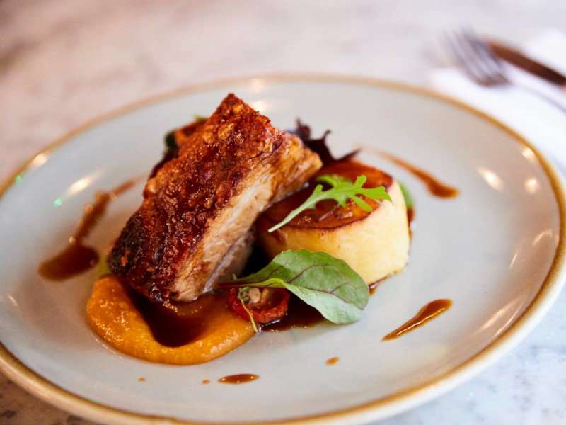 A delicious looking pork belly dish on a fancy white plate.