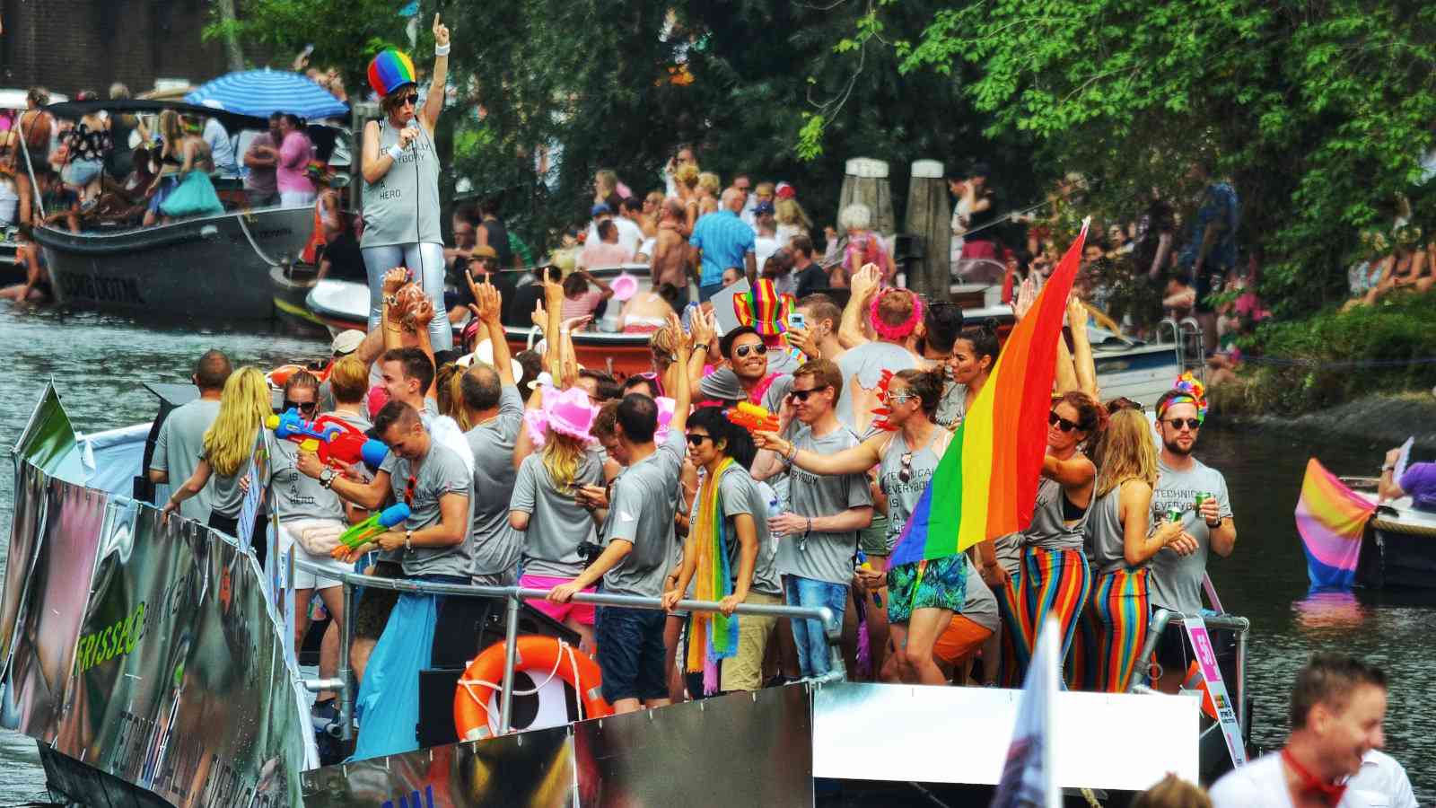 A boat full of people waving pride flags on the canals of Amsterdam.