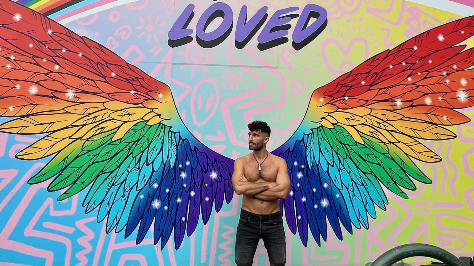 Gay man topless with rainbow angel wings street art on Oxford Street in Sydney.