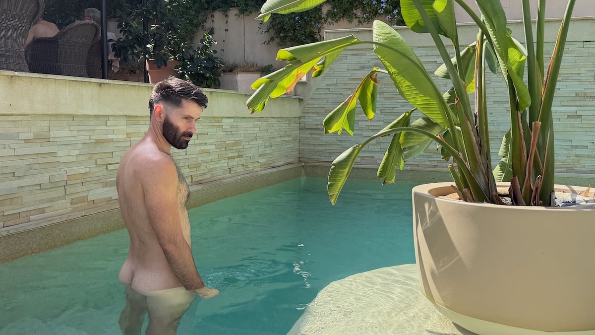 Seby naked in villa pool next to plant.