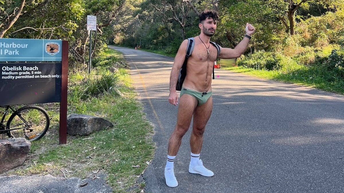 Gay guy hitchhiking in Speedos at Obelisk gay beach in Sydney.