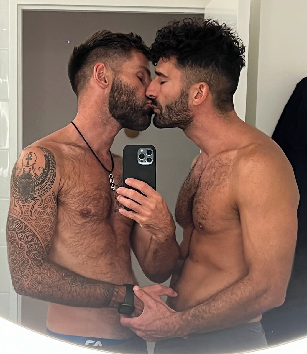 Romantic gay couple kiss in hotel room mirror.