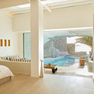 A white room leading into a small pool in a cave overlooking the sea.