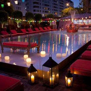 A swimming pool at night surrounded by red lounges and romantic lamps with floating lamps in the water as well.