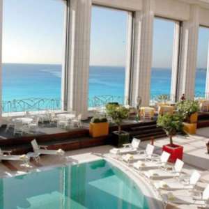 A swimming pool overlooking balcony colonnades with a view of the sea.