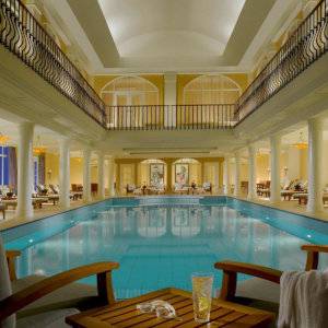 A luxurious indoor swimming pool with balconies above and fancy wooden seats around the edges.