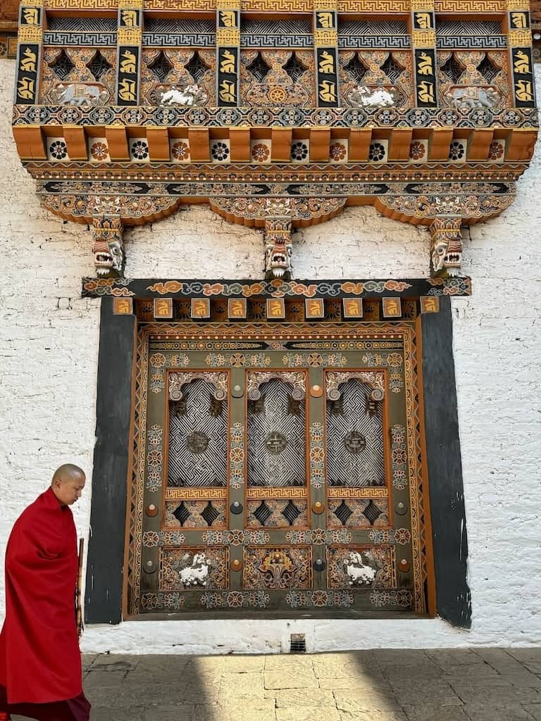 Beautiful Tibetan Bhutanese wall art at the Paro Dzong Monastery with monk walking in front of it.