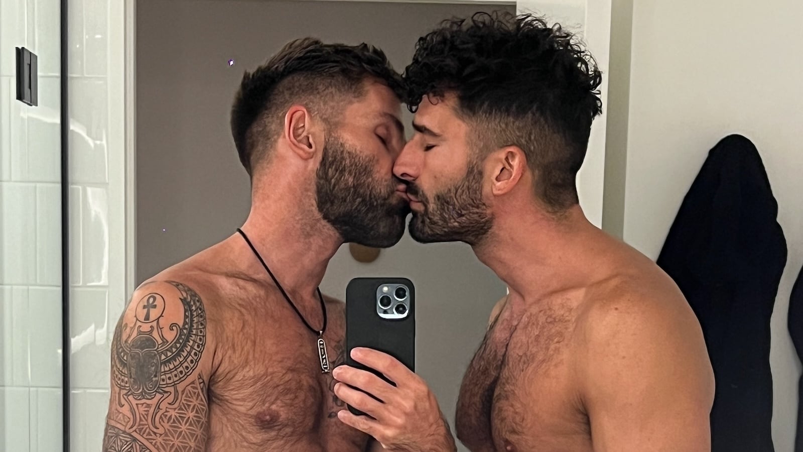 Gay couple kissing selfie in hotel mirror.