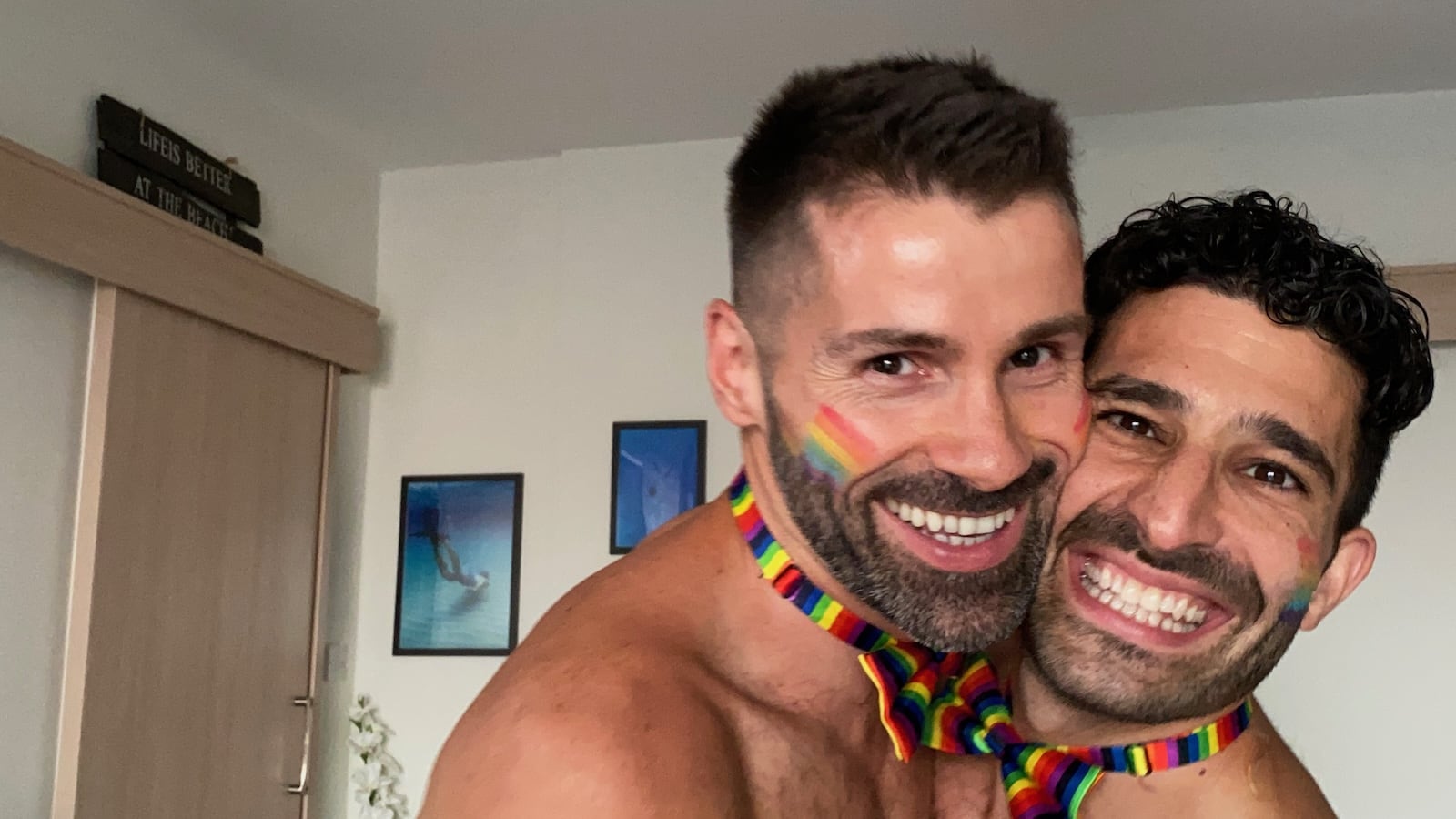 Gay couple smiling wearing rainbow bow ties.