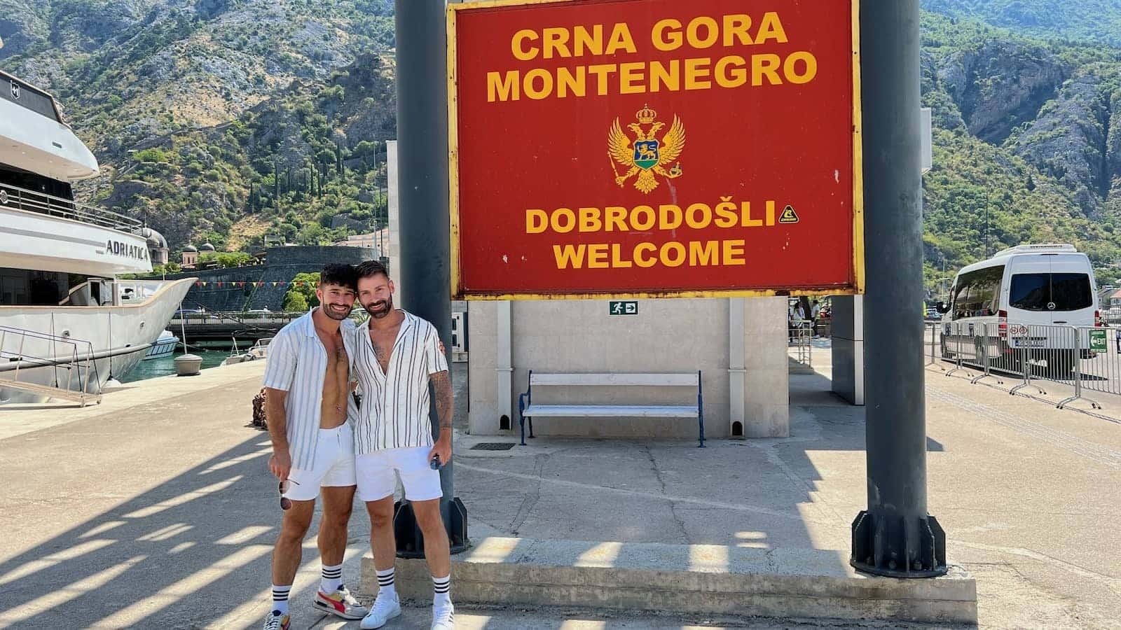 Gay couple with the Welcome to Montenegro sign in Kotor.