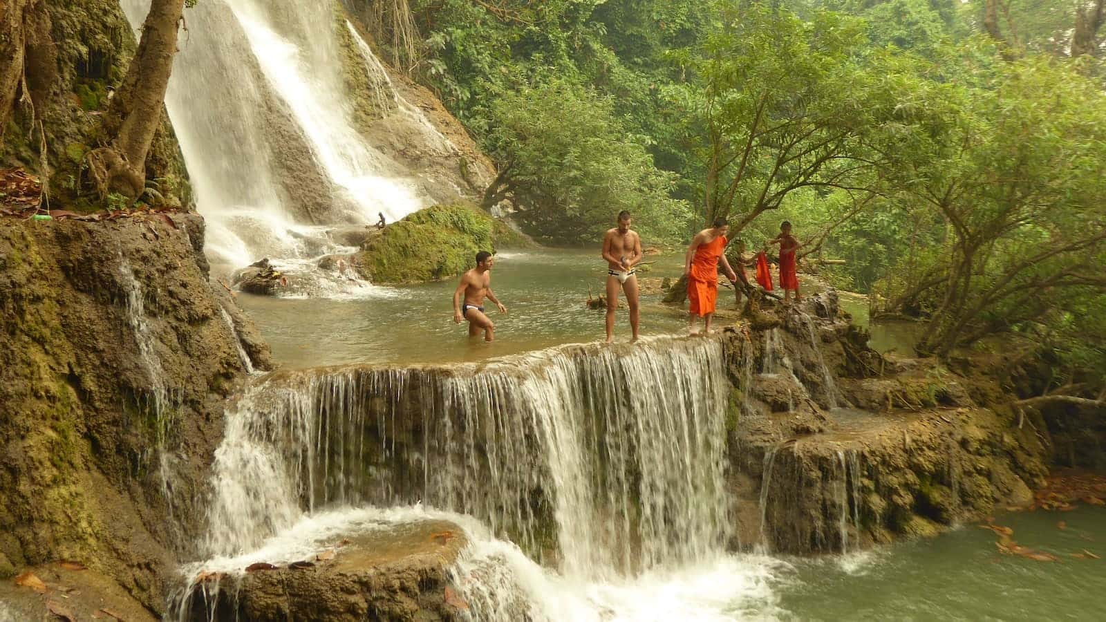 Diving with young monks in red robes at the Kiuang Si Falls in Luang Prabang in Laos.