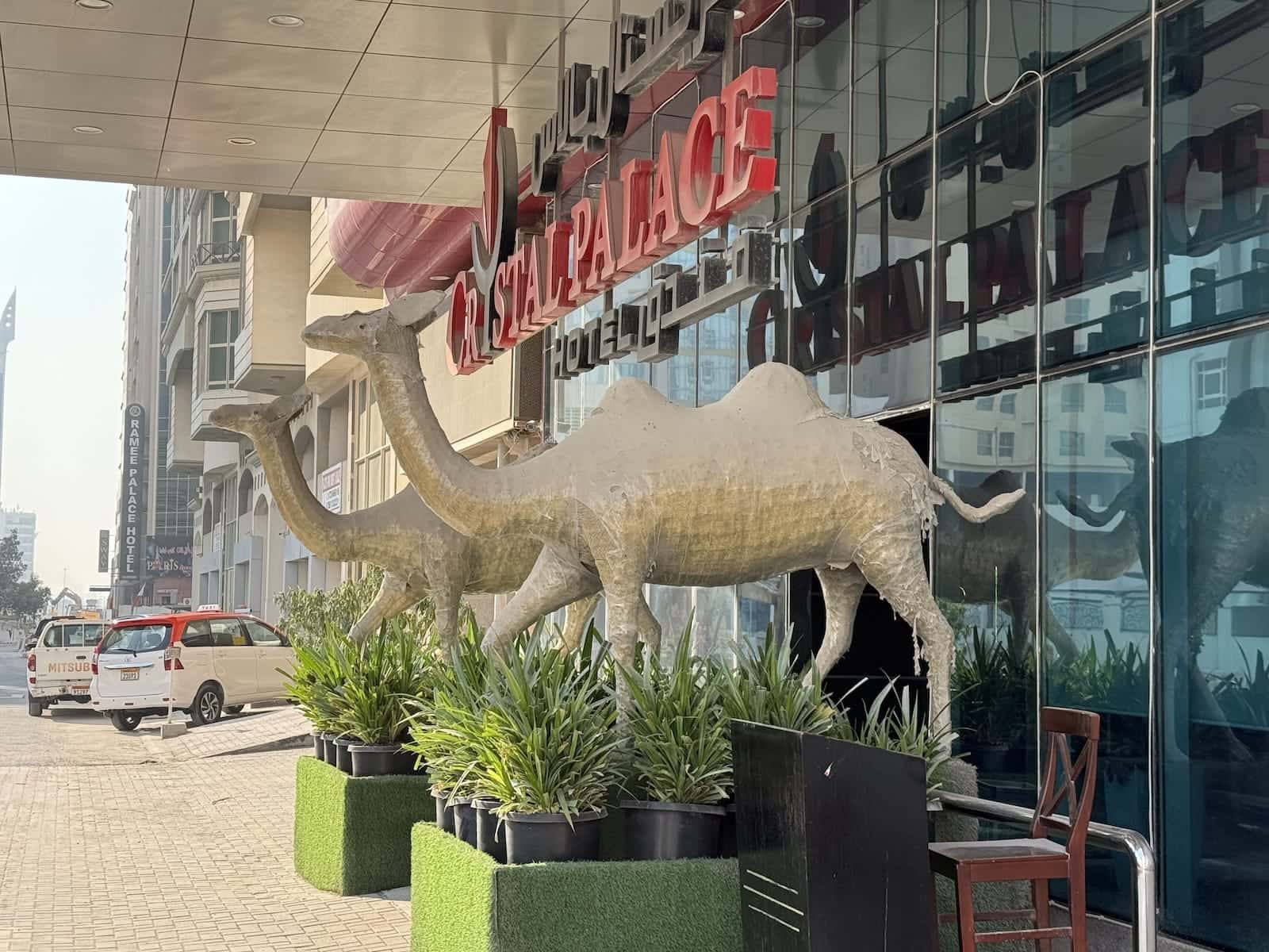 The front glass facade of a hotel called Crystal Palace, with camel statues in front of it.