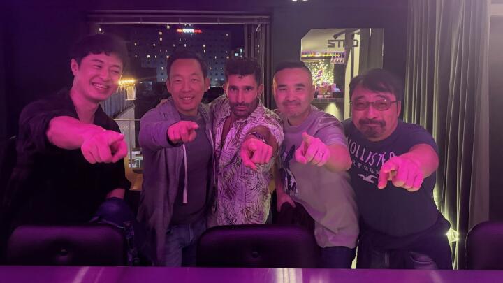 A group of men in a club pointing at the camera while illuminated in pink light.