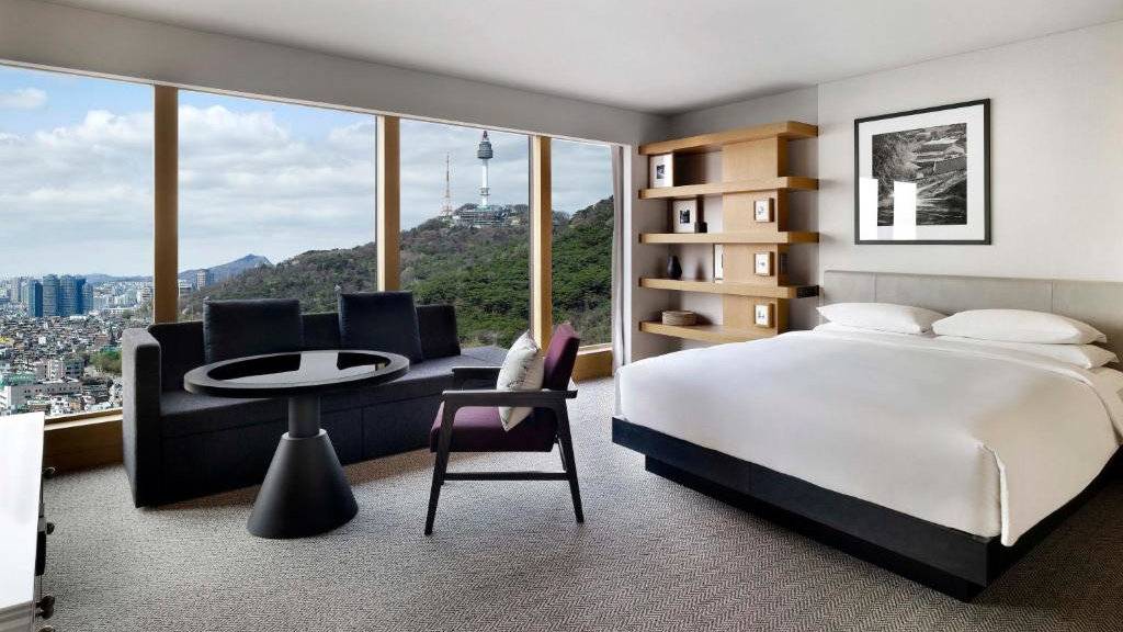 A spacious suite with a bed, couch, table and chair overlooking a sweeping view of Seoul at the Grand Hyatt Hotel.