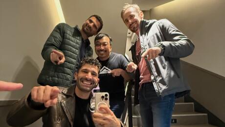 A group of guys on some interior stairs posing for a selfie and pointing down at the camera.