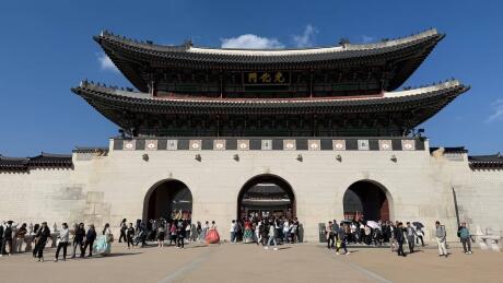 An impressive Korean palace with people walking around dwarfed by the giant structure.