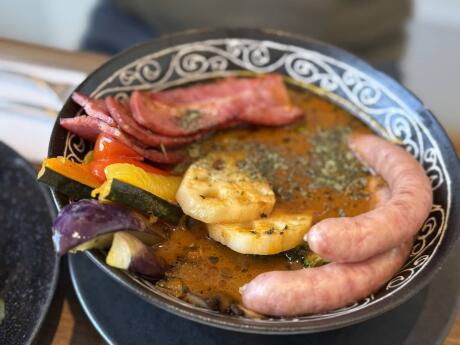 A close up shot of a bowl of curry with sausages and other meats and vegetables poking out of the liquid.