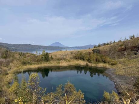 A landscape with a clear lake surrounded by greenery, a bay and a mountain in the distance behind it.