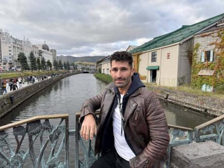 Stefan leaning on a fence with metal leaves and a canal with buildings alongside in the background.