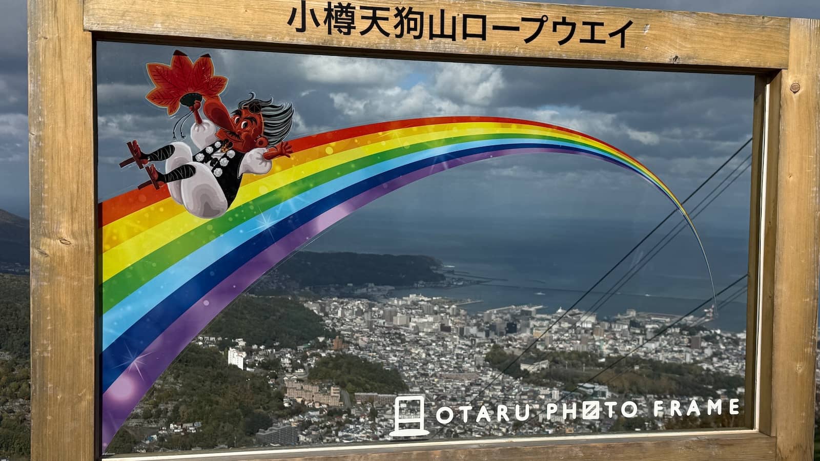 A frame and clear glass with a mascot on a rainbow looking out over Hokkaido.