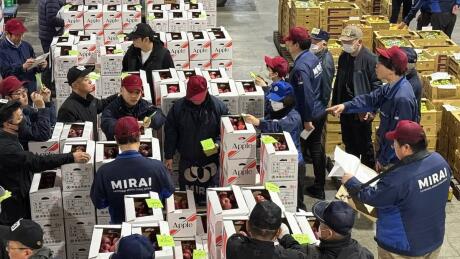 A group of Japanese men in a warehouse gathered around crates and boxes of apples.