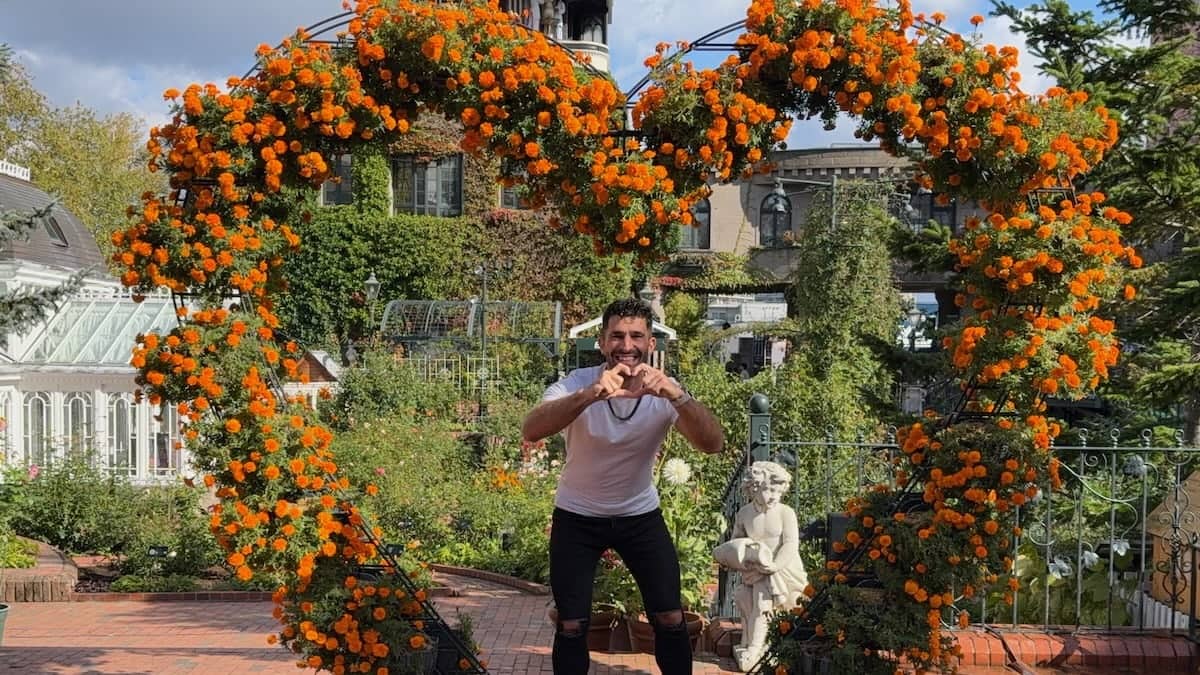 Stefan posing in a heart-shaped floral sculpture while also making a heart shape with his hands.