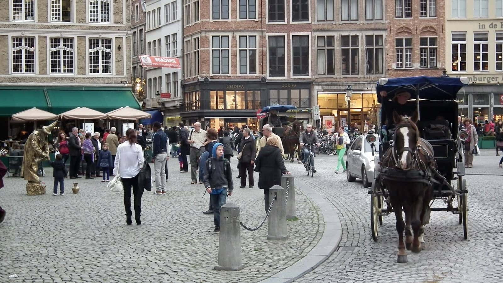 A street in Bruges with lots of people and a horse pulling a carriage.