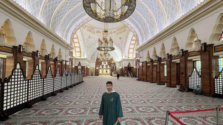 Stefan standing inside a spectacular mosque with patterned rugs and an opulent arched ceiling.