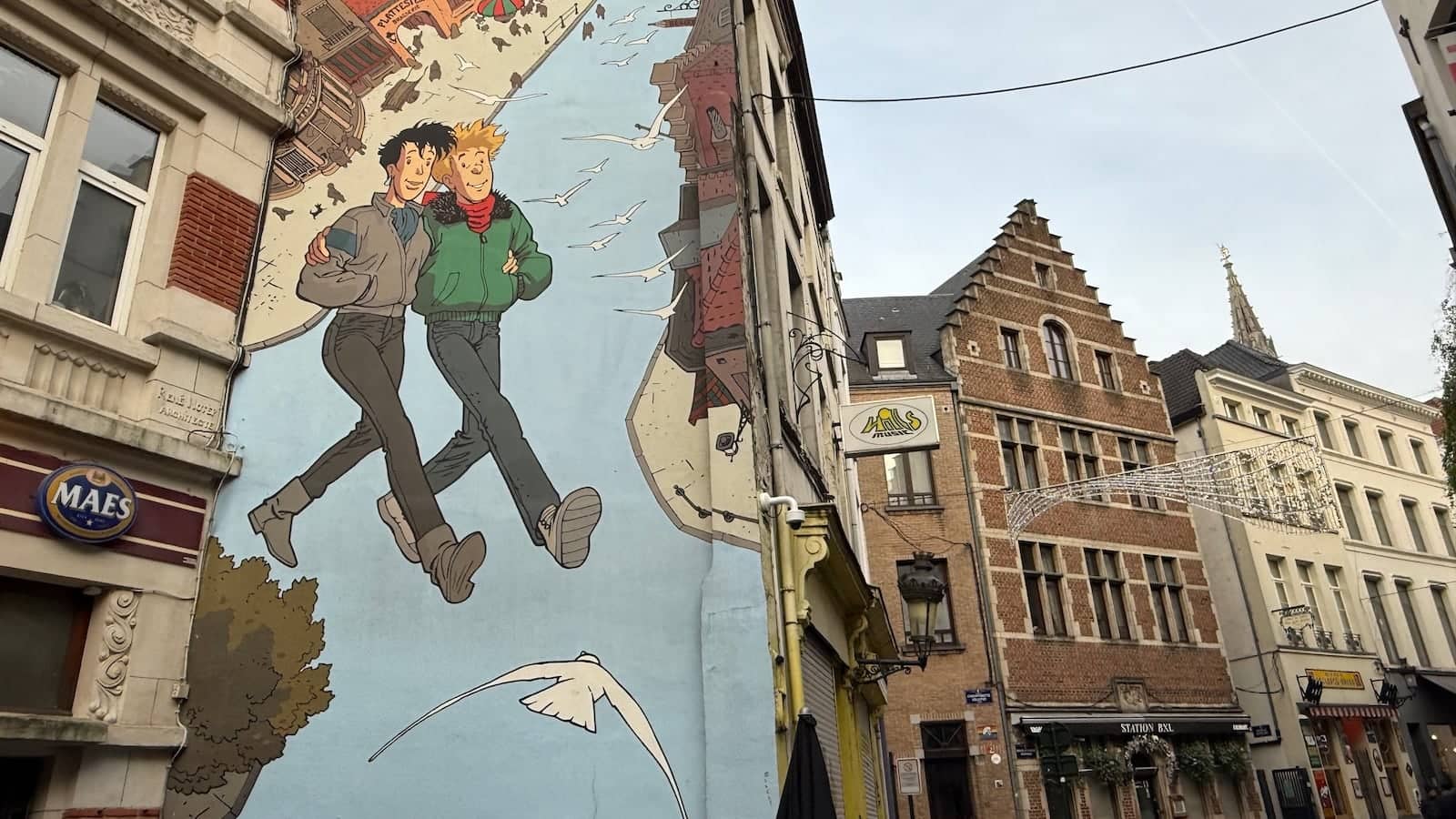 A street in Brussels with a massive mural of two men walking arm in arm on the side of a building.