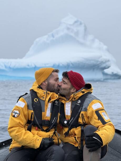 Gay couple kissing in front of Antarctica iceberg.