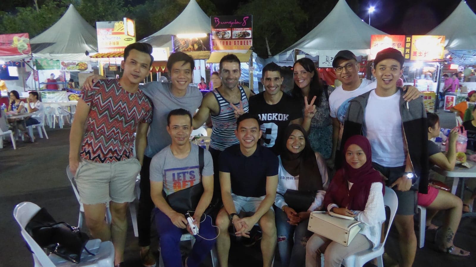 Seby and Stefan posing with a big group of other men at a night market.