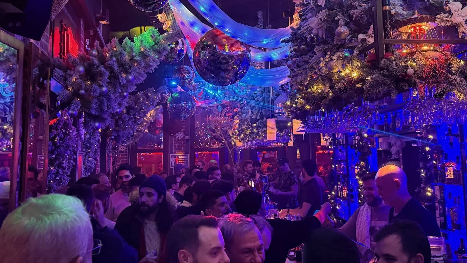 A packed dance floor at a bar with lots of purple and blue lighting.