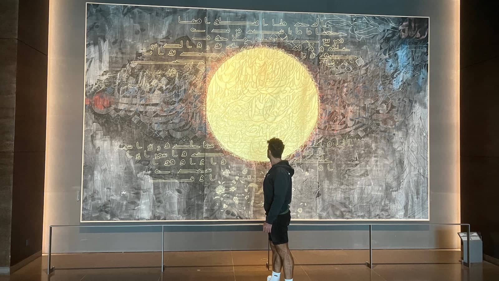 Stefan looking at a huge mural featuring a golden circle and Arabic writing on a grey background.