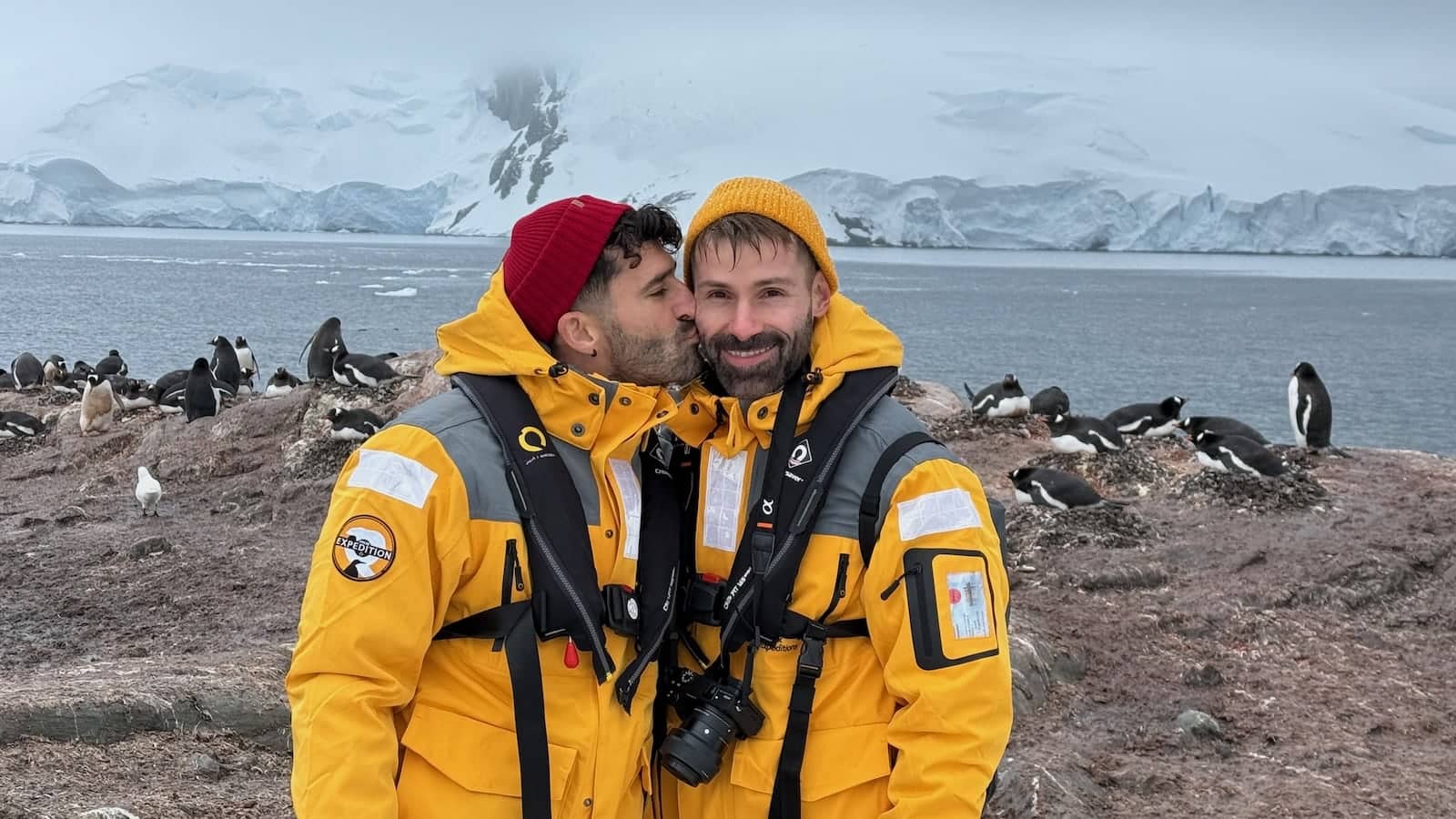 Stefan kissing Seby on the cheek in Antarctica in front of the penguins.