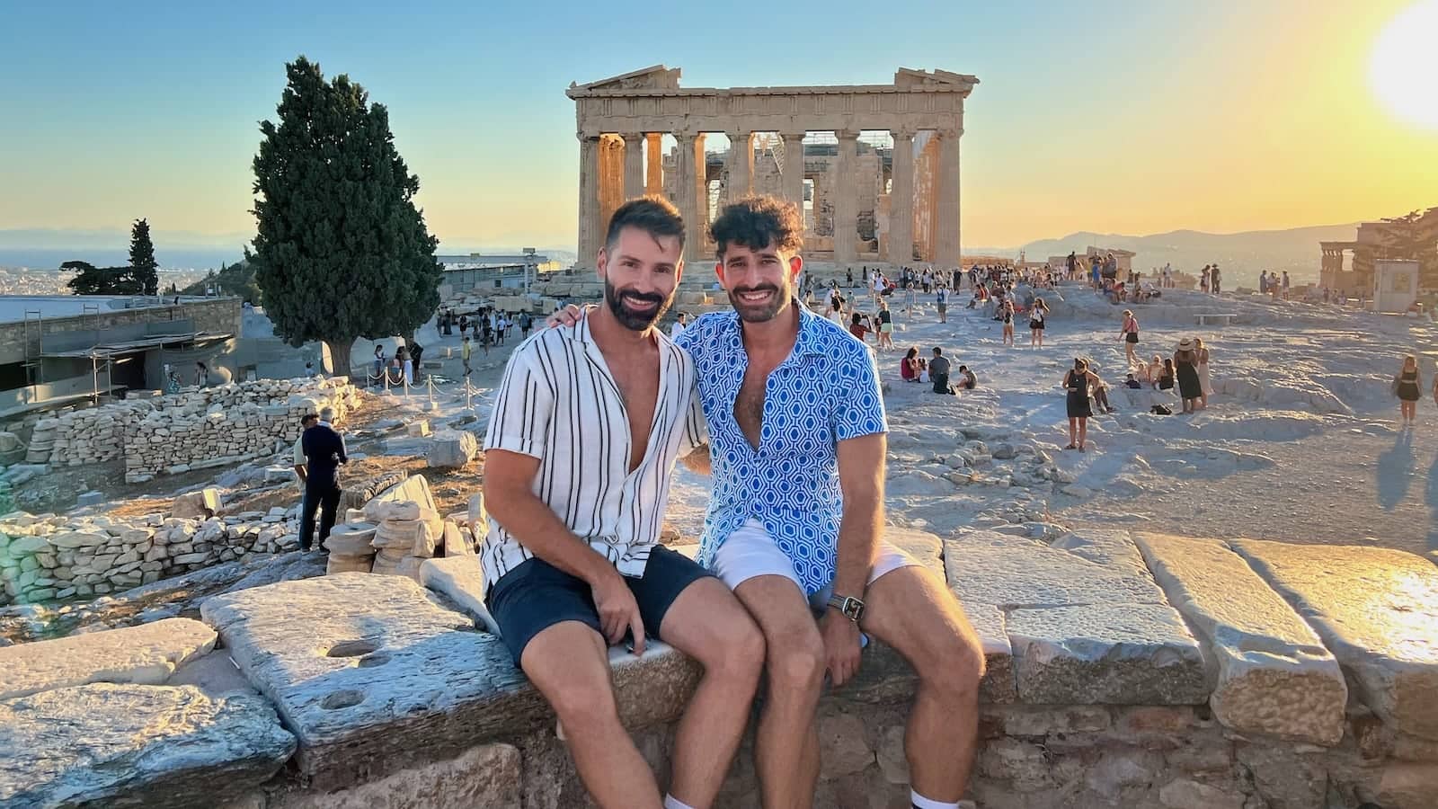 Stefan and Seby sitting on a rock wall with the Acropolis in Athens behind them at sunset.