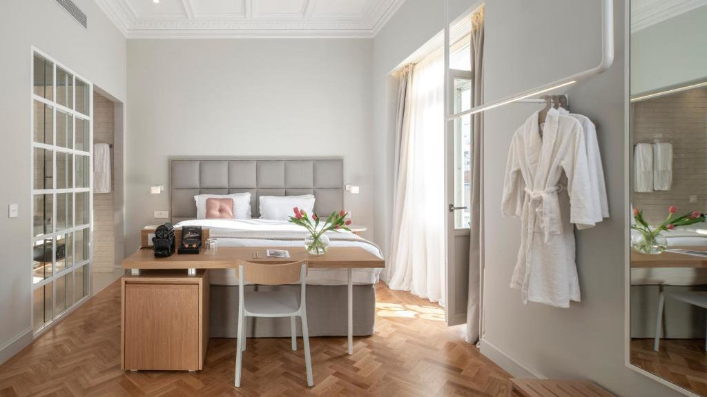 An airy hotel room with French doors open and white curtains flowing in the wind.