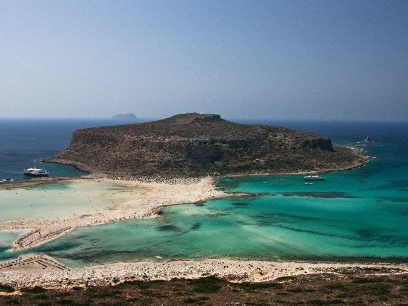 An island seen from a hill with sandy beaches and azure waters.