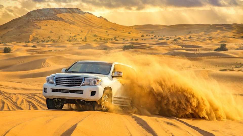 A white 4wd car driving through sand dunes.