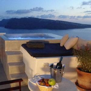 A hot tub in white stone overlooking ocean and an island at dusk.