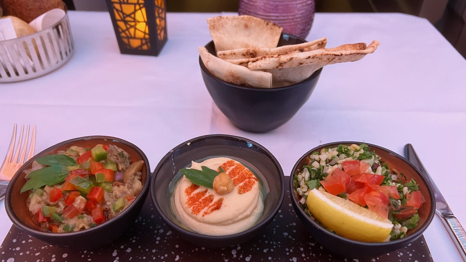 3 small bowls containing different dips on a table, as well as a bowl with flatbread.