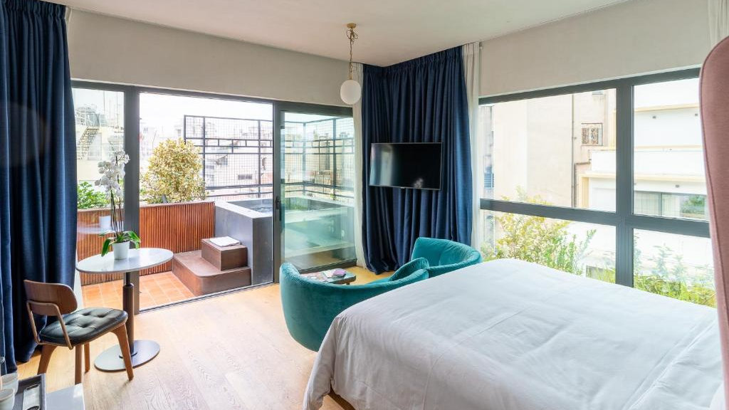 A hotel room with a private balcony featuring a jacuzzi and a cute blue couch at the end of the bed.