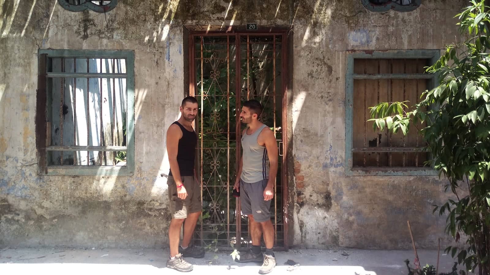 Seby and Stefan standing next to a rusty gate in a run-down wall.