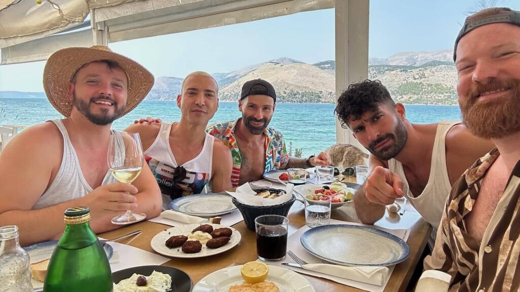 A group of guys smiling at a tale with food and ocean in the background.